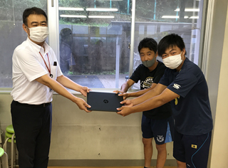 運搬を手伝ってくださった栄徳高等学校 生徒の方々に
パソコンを手渡す当社総務部長 小池（左）